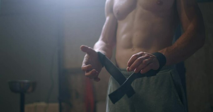 Young athletic Caucasian man changing, putting weight lifting straps on in gym locker room before workout slow motion. ties arms to barbell with fitness straps. 