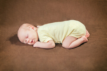 Beautiful newborn baby boy sleeping peacefully on the soft brown blanket