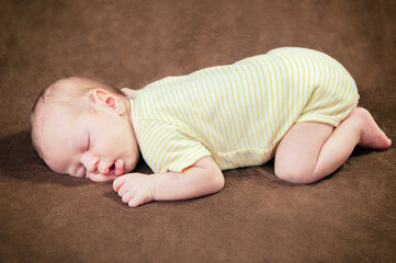 Beautiful newborn baby boy sleeping peacefully on the soft brown blanket