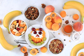 Fototapeta na wymiar Useful breakfast with ingredients, food for children, fruit salad with granola, apricots, bananas, honey and peaches on a bright table. The concept of a healthy and natural diet, lifestyle,