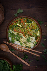 Vegan Thai green curry and rice noodles served in wooden bowl on wooden table