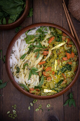 Vegan Thai green curry and rice noodles served in wooden bowl on wooden table