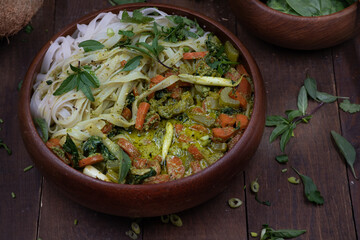 Vegan Thai green curry and rice noodles served in wooden bowl on wooden table