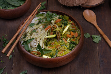Vegan Thai green curry and rice noodles served in wooden bowl on wooden table