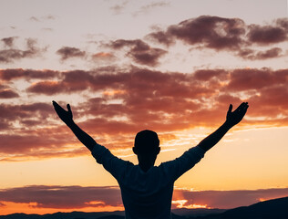 Young man rising up the hands and greeting the stunning sunset orange-pink sky colors over the mountain landscape back view. New life, new day beginning, or success concept image. © Soloviova Liudmyla