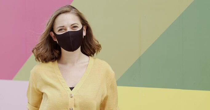 Portrait of pretty female wearing protective face mask looking at camera happy with multi coloured background