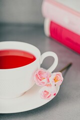 Raspberry tea, pink freesia flowers and books on a gray background, toned