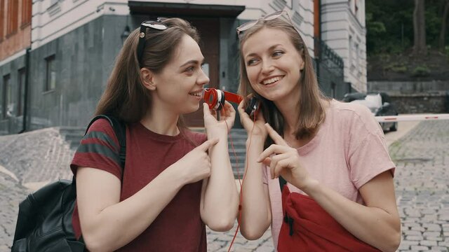 Two girls friends sharing red headphones to listen to the music