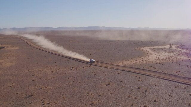 Aerial drone shot of rally car racing along a dirt track road with trails of dust and smoke in the middle of the desert during the Africa eco race or Dakar Rally