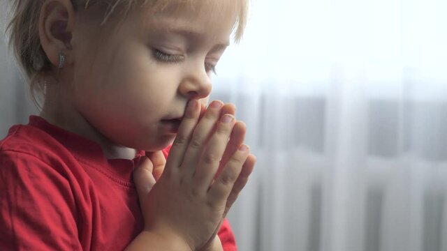 little daughter girl makes a wish prayers bedtime religion concept . prayer child indoors praying by bed front of lifestyle window