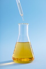 Vertical closeup of a dropper over an Erlenmeyer flask with yellow liquid on a blue background