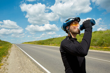 A professional road cyclist stopped to drink water on an open road on a clear summer day