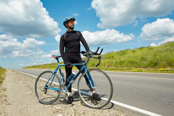A professional road cyclist stopped to rest on an open road on a clear summer day