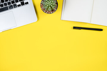 Top view of laptop, cactus, and notebook on yellow background