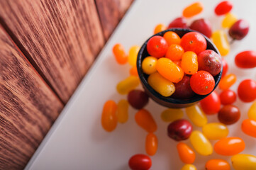 Various colorful cherry tomatoes on white and wooden background. Creative design, beautiful lighting.