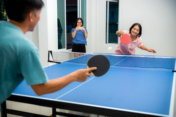 Couple fun playing table tennis or Ping pong indoor together leisure with competing in sports games at house. Father mother and daughter Asian family enjoy recreation exercise stay at home in Thailand