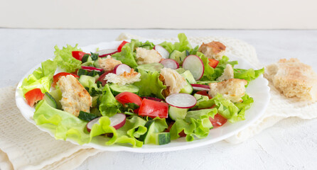 Fattoush salad with tomato, cucumber, radish and toasted pita bread, oil spilled in a white plate on a napkin. Vegetarian salad with vegetables and bread