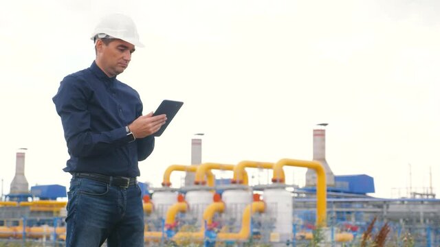 engineer man power and energy using digital tablet. worker in a helmet works at an oil-gas plant. lifestyle engineer studies documents business industry
