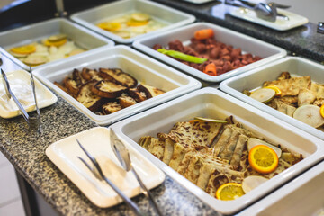 Decorated breakfast catering setting at the hotel, with variety of dishes: cereal, corn flakes, vegetables, toast, pancakes, pastry, cupcakes and other food