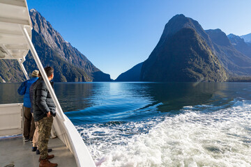 Male tourists on board a cruise boat in Milford Sound look back towards Mitre Peak, Fiordland National Park, New Zealand