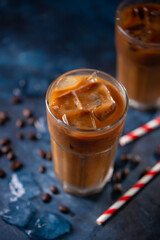Iced coffee in a glass with cream, or milk and coffee beans. Cold summer drink on a blue background