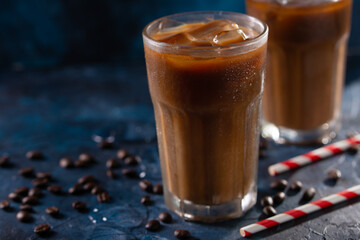 Cold coffee with ice cubes and milk on a background with coffee grains and tubes, dark blue background, summer, cool drinks