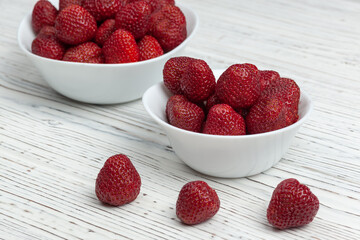 two white plates with strawberries on a wooden background, next to lie three strawberries