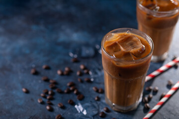 Ice cold coffee with ice cubes and coffee grains on a blue background. Cold summer drink with pipes