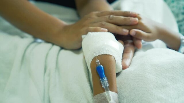 Young mother is holding hand bandaged of little daughter with comforting while they lying in the hospital bed sleeping. Recovering little girl. Hopeful emotional moment in ward. Focus on the hands.