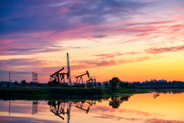 Obraz premium Oil Pumping Unit by the lake in the sunset.