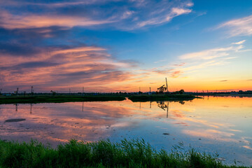Oil Pumping Unit by the lake in the sunset.