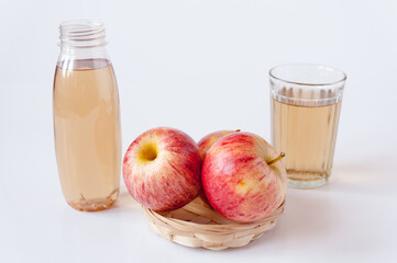 Three red apples in a wicker plate, a glass and a bottle of Apple juice on a white background