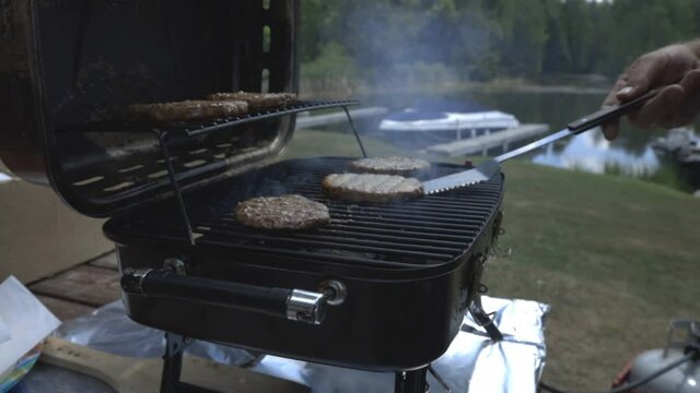 Man Grilling A Delicious Burger Steaks Into The Barbeque Griller Near The Kawartha Lakes In Ontario, Canada.  - close up