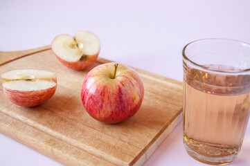 Whole and cut red Apple on a wooden Board and a glass of Apple juice on a pink background