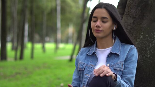 Mujer joven caucasica escucha musica tranquilamente en un parque, disfrutando del dia y el ambiente. Plano medio