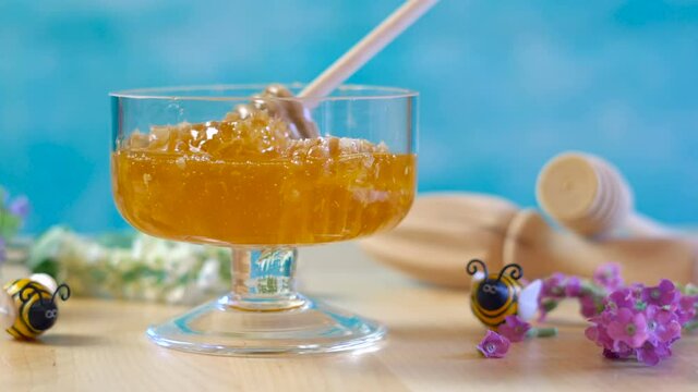 Raw honeycomb with liquid honey in glass jar with lavendar on blue background.