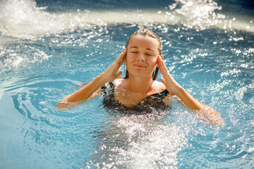 Pretty ypung rtourist woman touches her head with her hand while swim in the swimming pool. Spa treatment, calmness concept