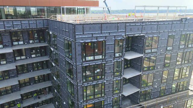 exterior of an building still in construction, windows installed but still undone, workers on the roof and balconies