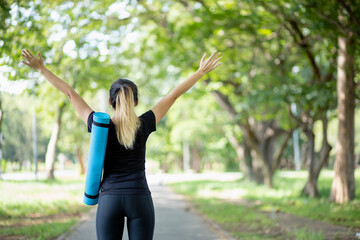 Asian women holding yoga mats are going to do yoga at the park to stay healthy and have good shape.