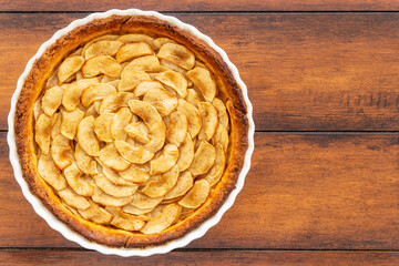 Homemade baked French apple tart, an open faced apple pie, in a baking white ceramic dish on a...