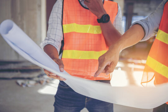 Structural engineer and architect working with blueprints discuss at the outdoors building construction site.
