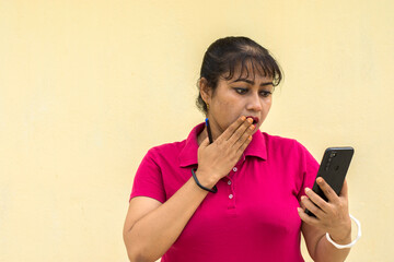 Indian female model looking at mobile phone surprise face in yellow background with copy space for text