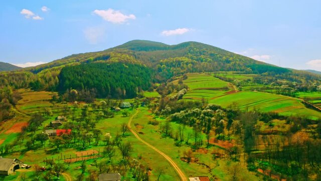 drone flies above small village on the background beautiful mountains with forest sunny daytime with blue sky