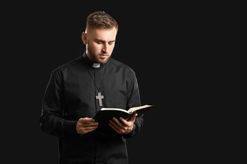 Young priest with Bible on dark background