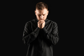 Young priest praying to God on dark background