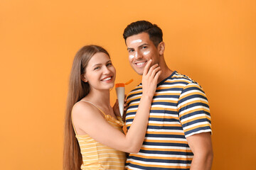 Young couple applying sunscreen cream against color background