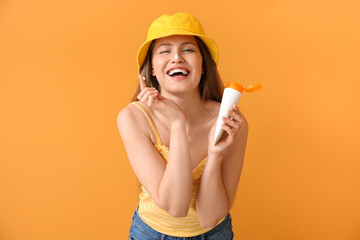 Young woman applying sunscreen cream against color background