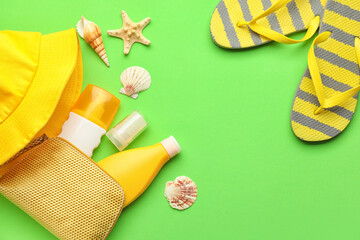 Bag with sunscreen cream, hat and flip-flops on color background