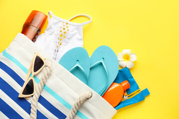 Bag with sunscreen cream and supplies on color background