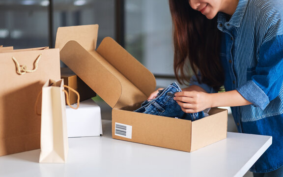 A beautiful young asian woman receiving and opening a postal parcel box of clothing at home for delivery and online shopping concept